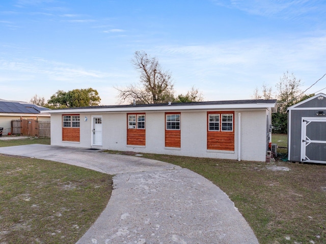 ranch-style house with concrete driveway, fence, an outdoor structure, a shed, and a front yard