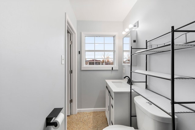 bathroom with toilet, speckled floor, vanity, and baseboards