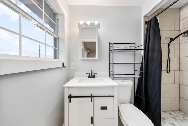 bathroom with toilet, tiled shower, and vanity