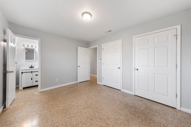 unfurnished bedroom with light speckled floor, visible vents, baseboards, and ensuite bathroom