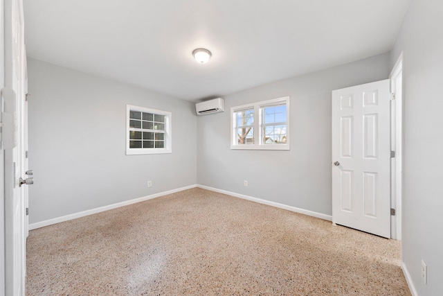 empty room with a wall unit AC, baseboards, and light speckled floor