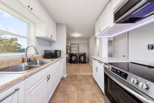 kitchen featuring appliances with stainless steel finishes, washing machine and clothes dryer, light countertops, white cabinetry, and a sink