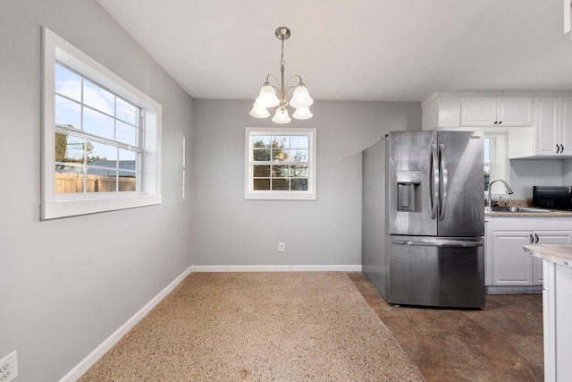 kitchen with light countertops, hanging light fixtures, white cabinets, a sink, and stainless steel fridge