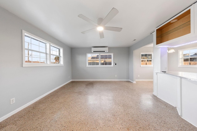 unfurnished room with ceiling fan, baseboards, light speckled floor, and a wall mounted AC