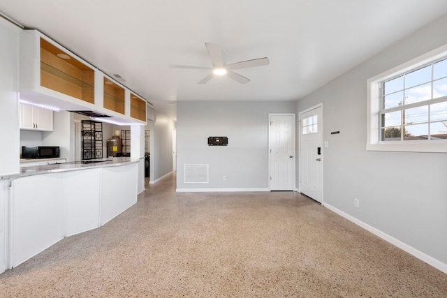 interior space with ceiling fan, light speckled floor, visible vents, and baseboards