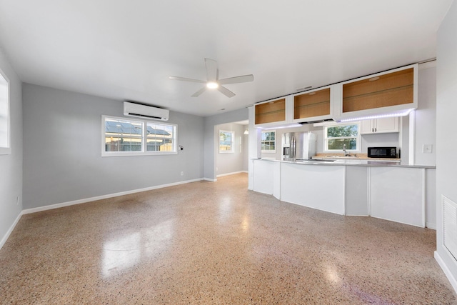 kitchen featuring stainless steel fridge, white cabinets, a wall mounted air conditioner, black microwave, and a sink