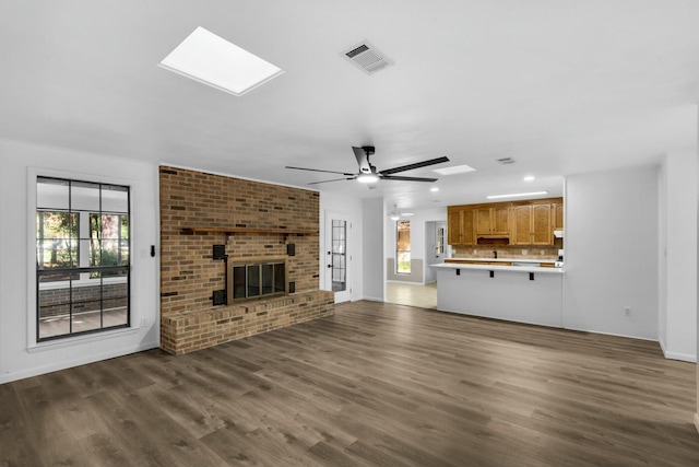 unfurnished living room featuring dark wood-style floors, a skylight, a brick fireplace, and visible vents