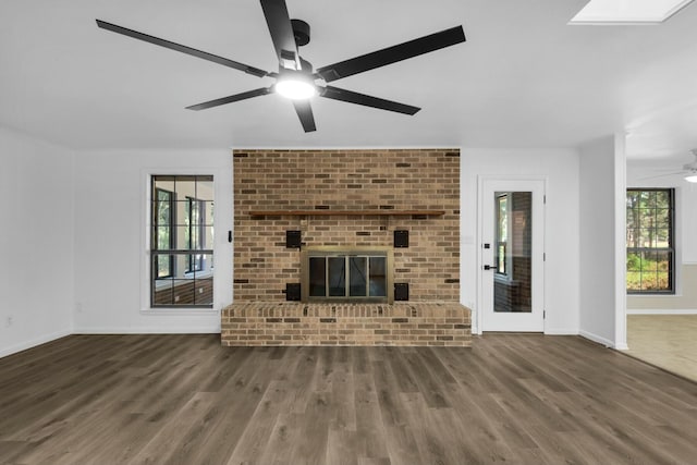 unfurnished living room with a wealth of natural light, a brick fireplace, and wood finished floors