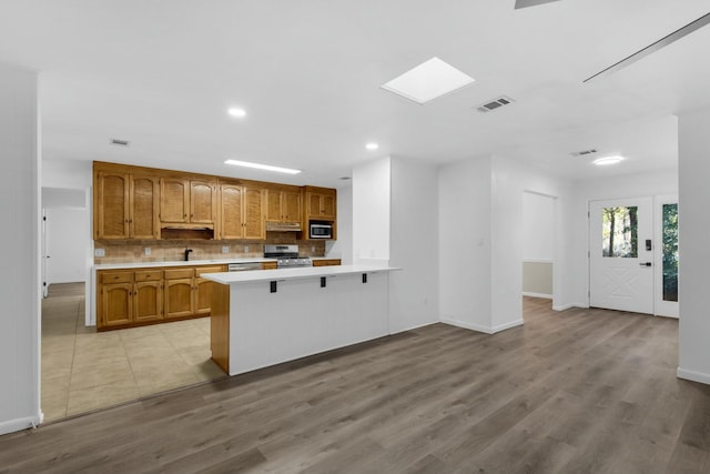 kitchen with under cabinet range hood, a peninsula, visible vents, light countertops, and appliances with stainless steel finishes