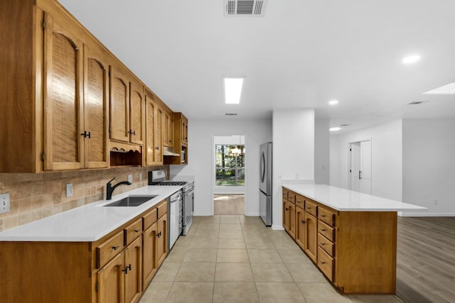 kitchen featuring visible vents, appliances with stainless steel finishes, a peninsula, a sink, and backsplash