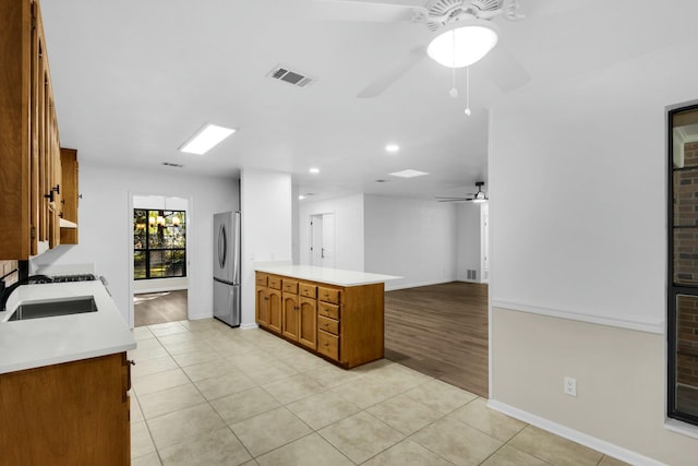 kitchen with light countertops, visible vents, brown cabinetry, freestanding refrigerator, and a sink