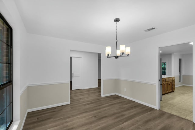 empty room with baseboards, a notable chandelier, visible vents, and wood finished floors