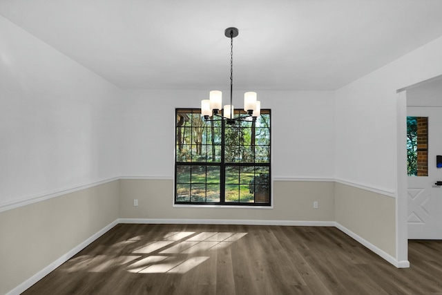 unfurnished dining area with baseboards, an inviting chandelier, and wood finished floors