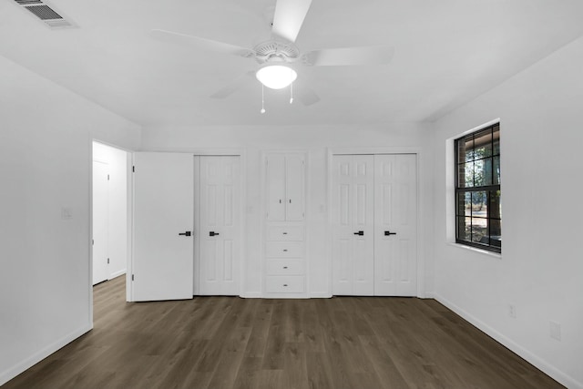 unfurnished bedroom with baseboards, dark wood finished floors, visible vents, and multiple closets