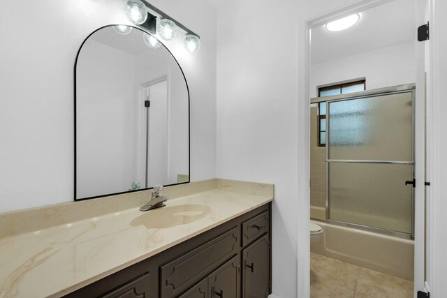 bathroom with toilet, shower / bath combination with glass door, tile patterned flooring, and vanity