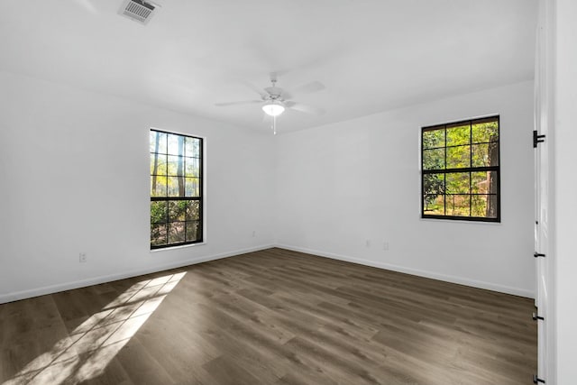 empty room featuring wood finished floors, visible vents, and a healthy amount of sunlight