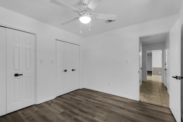 unfurnished bedroom with dark wood-style floors, ceiling fan, visible vents, and baseboards