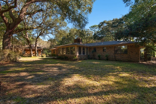 back of property featuring brick siding, a yard, and a chimney