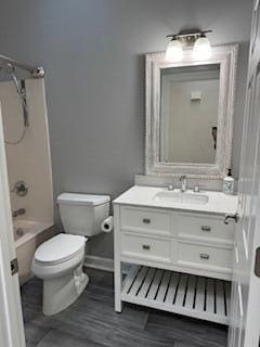 full bath with baseboards, toilet, wood finished floors, tub / shower combination, and vanity