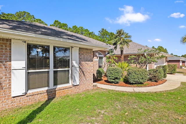 entrance to property with a garage, driveway, a shingled roof, a yard, and brick siding