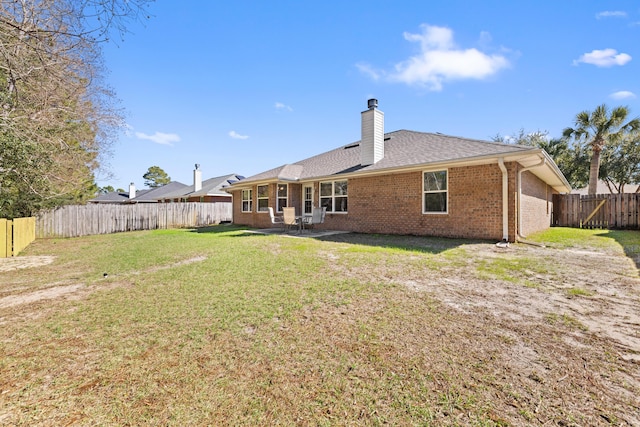 back of property with a fenced backyard, a chimney, roof with shingles, a yard, and brick siding