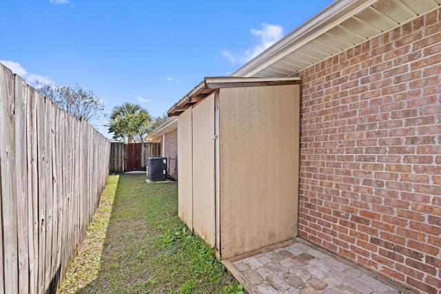 view of side of home featuring a fenced backyard, a lawn, central AC, and brick siding