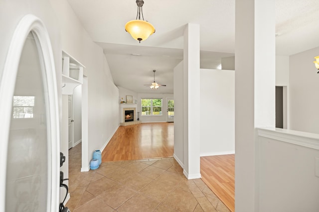 foyer entrance with a warm lit fireplace, light tile patterned floors, baseboards, a ceiling fan, and lofted ceiling