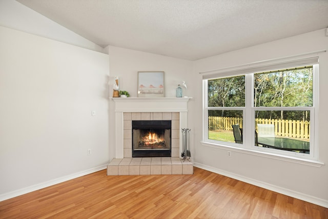 unfurnished living room with lofted ceiling, wood finished floors, a tile fireplace, and baseboards