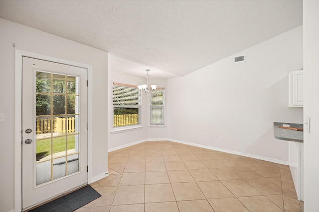 unfurnished dining area with light tile patterned floors, visible vents, an inviting chandelier, a textured ceiling, and baseboards