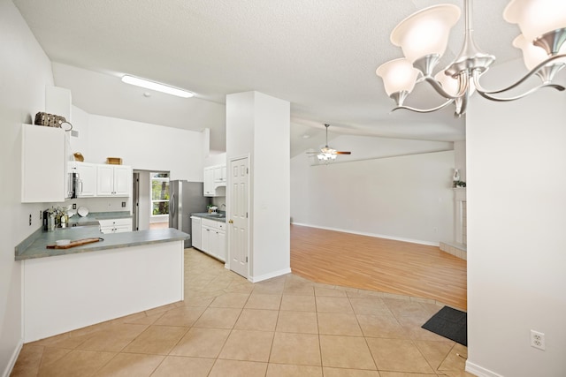 kitchen featuring lofted ceiling, light tile patterned flooring, ceiling fan with notable chandelier, stainless steel appliances, and white cabinets