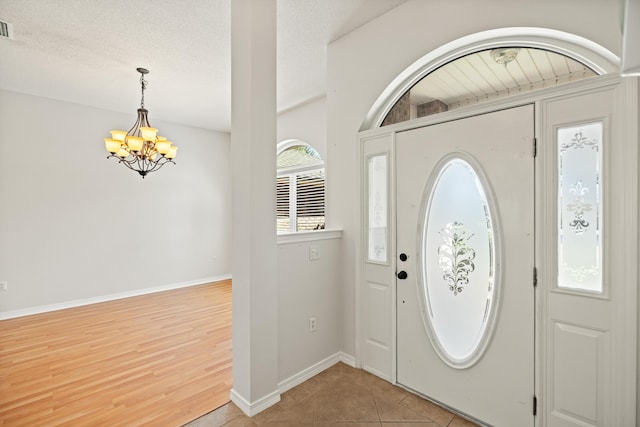 foyer entrance with light tile patterned floors, visible vents, a textured ceiling, a chandelier, and baseboards