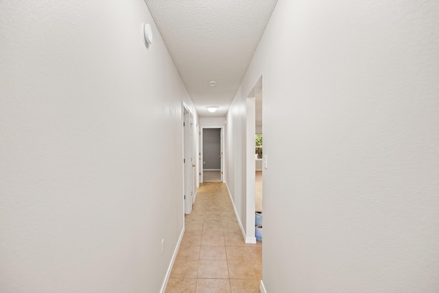 corridor with light tile patterned floors, baseboards, and a textured ceiling