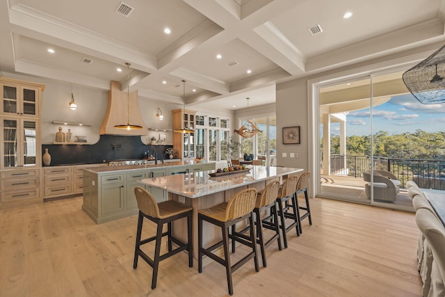 kitchen featuring beamed ceiling, visible vents, light wood-type flooring, coffered ceiling, and a large island with sink