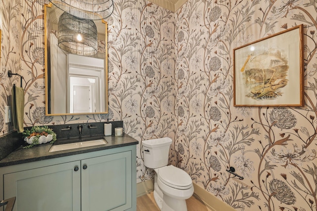 half bathroom featuring vanity, toilet, and wallpapered walls