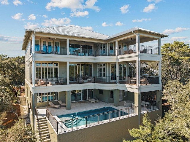 rear view of house with metal roof, a balcony, a ceiling fan, a fenced in pool, and a patio area