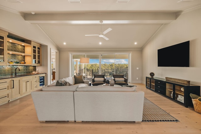 living area featuring beverage cooler, lofted ceiling with beams, light wood-style flooring, ornamental molding, and wet bar