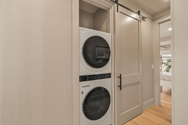 washroom featuring light wood-style floors, stacked washer / drying machine, laundry area, and a barn door