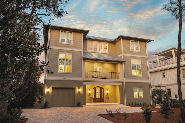 view of front of house featuring a garage, decorative driveway, brick siding, and a balcony