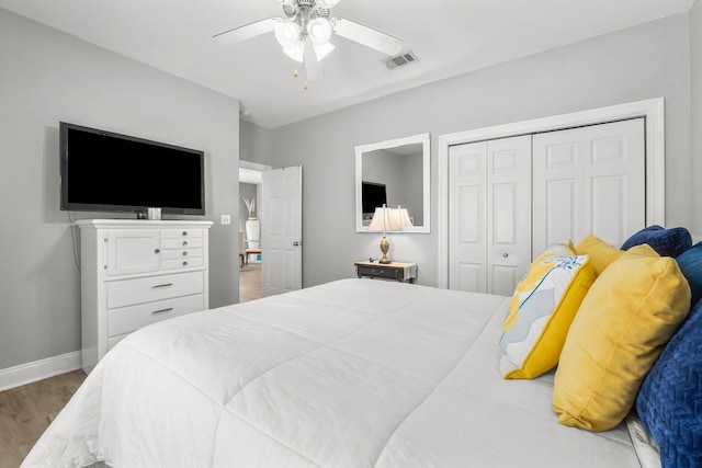 bedroom with baseboards, visible vents, ceiling fan, wood finished floors, and a closet