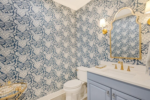 half bathroom with toilet, ornamental molding, vanity, and wallpapered walls