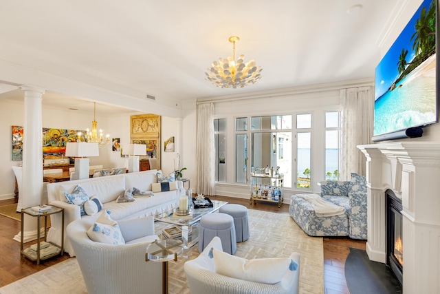 living area with an inviting chandelier, decorative columns, wood finished floors, and a glass covered fireplace