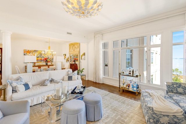 living area with decorative columns, baseboards, visible vents, wood finished floors, and a notable chandelier