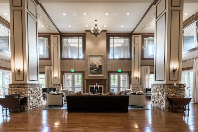 living area with a notable chandelier, a fireplace, wood finished floors, a towering ceiling, and crown molding