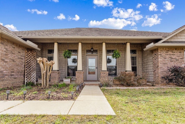 property entrance with covered porch, brick siding, and roof with shingles