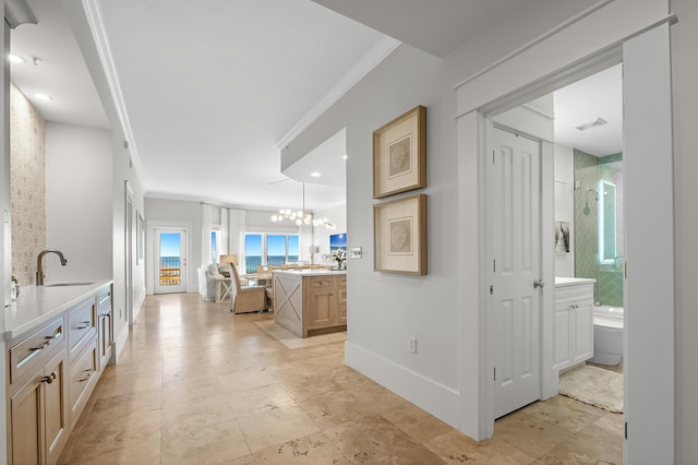 hallway featuring a chandelier, a sink, visible vents, baseboards, and crown molding