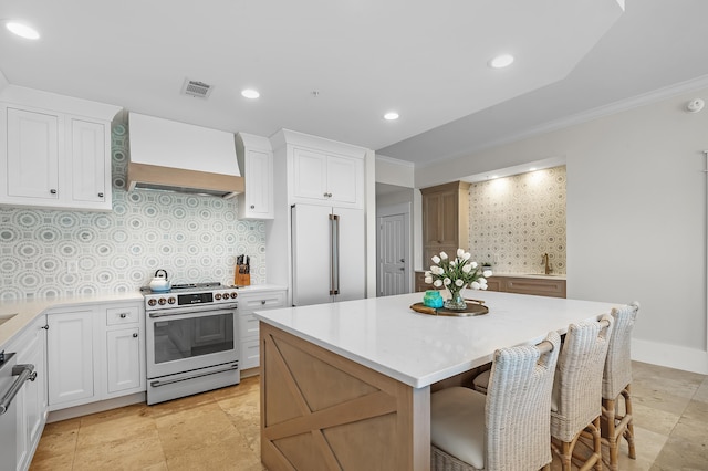 kitchen featuring electric range, custom exhaust hood, light countertops, white cabinetry, and built in fridge