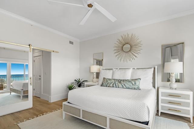 bedroom with a barn door, baseboards, ceiling fan, wood finished floors, and crown molding