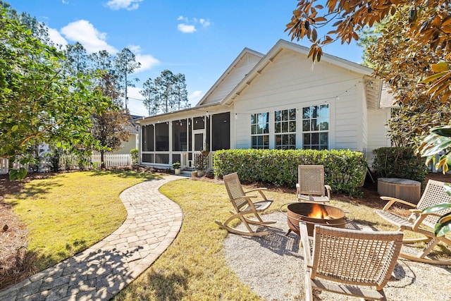 back of property featuring a fire pit, a yard, fence, and a sunroom