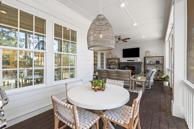 sunroom / solarium featuring a ceiling fan and a warm lit fireplace