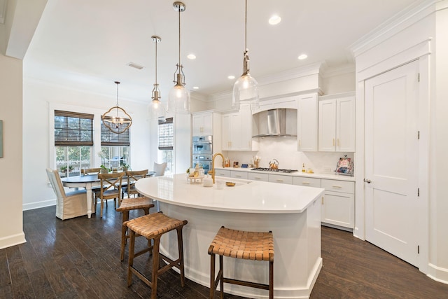 kitchen featuring double oven, a sink, gas stovetop, a kitchen breakfast bar, and wall chimney range hood